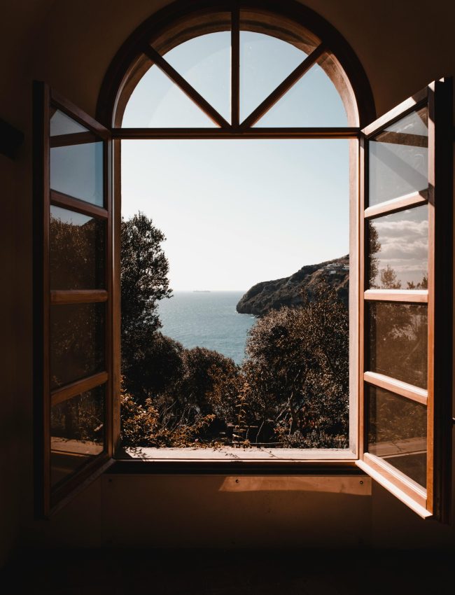 Elegant arched window view of a serene ocean landscape with lush greenery.